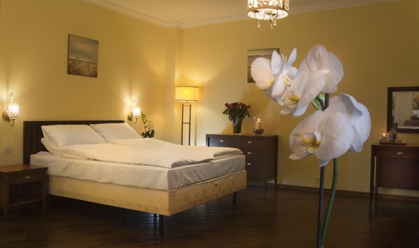A hotel room with a bed, bedside lamps, a nightstand, a dresser, a mirror, and a large orchid plant.