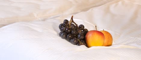 Ein ordentlich bezogenes Bett mit weißer Bettdecke, einer Topforchidee und einer Obstschale auf dem Bett.