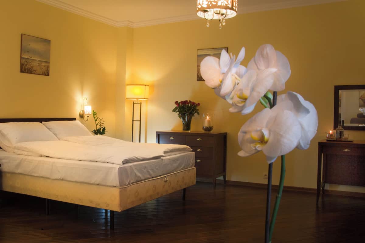 Une chambre d’hôtel comprenant un lit, des lampes de chevet, une table de nuit, une commode, un miroir et une grande plante d’orchidée.