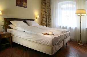 A neatly made bed with a tray of pastries and a cup of coffee, a bedside table with a lamp, and a floral curtain.