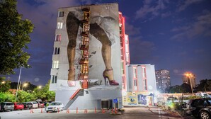 A building with a mural of high-heeled shoes, a fire escape, and a parking lot with cars. - Art Hotel Simona (Sofia)