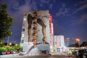 Um edifício com um mural de sapatos de salto alto, escada de incêndio e um estacionamento com carros.