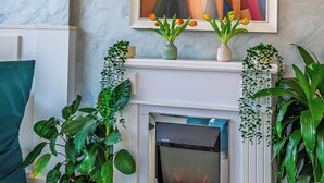 A living room with a fireplace, a painting, and potted plants. - Art Hotel Simona (Sofia)