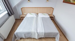 A twin bed with a wooden headboard, a bedside table, and a window with curtains. - Antica Residence (Kraków)