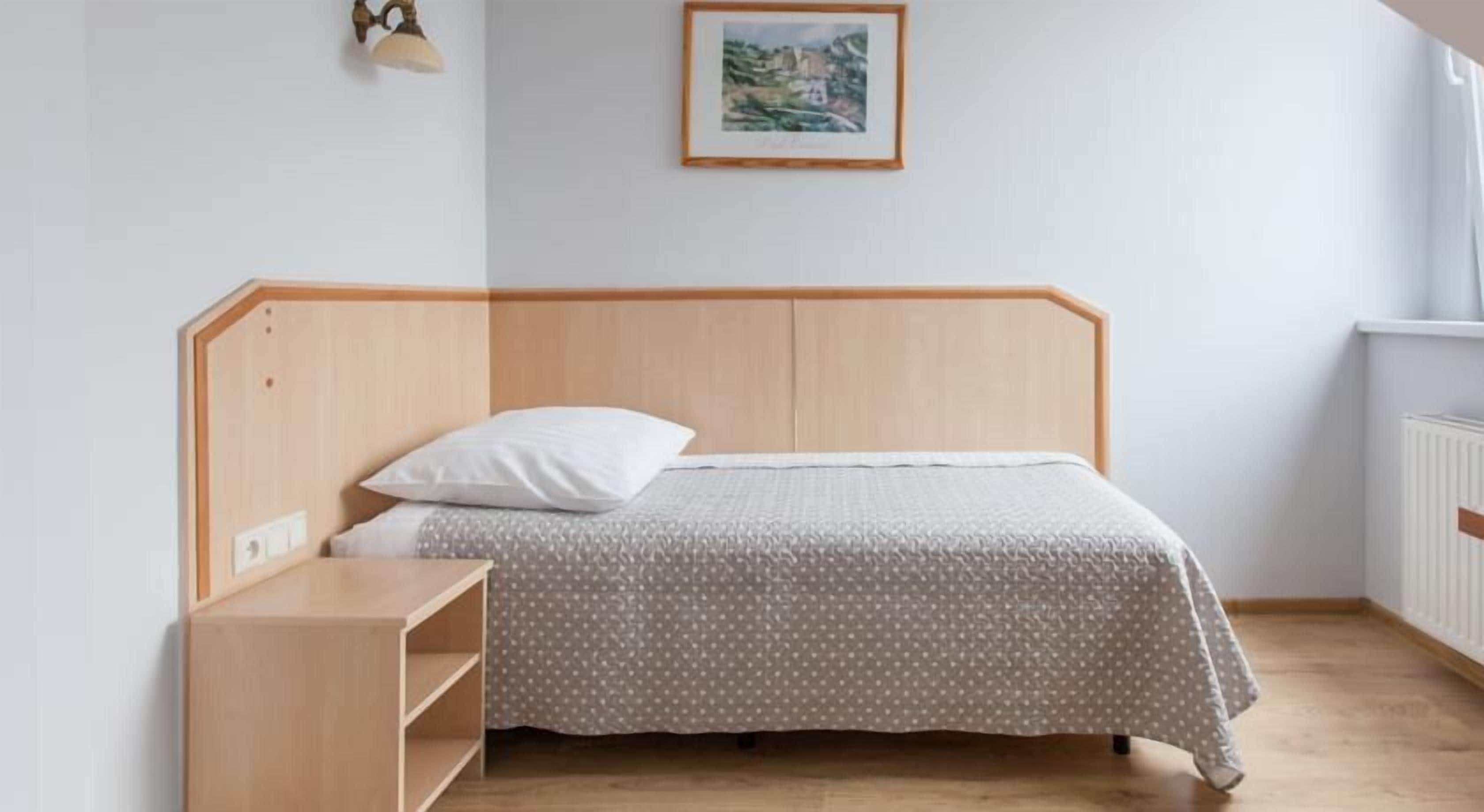 Uma cama de solteiro com cabeceira de madeira, mesa de cabeceira e luminária na parede.
