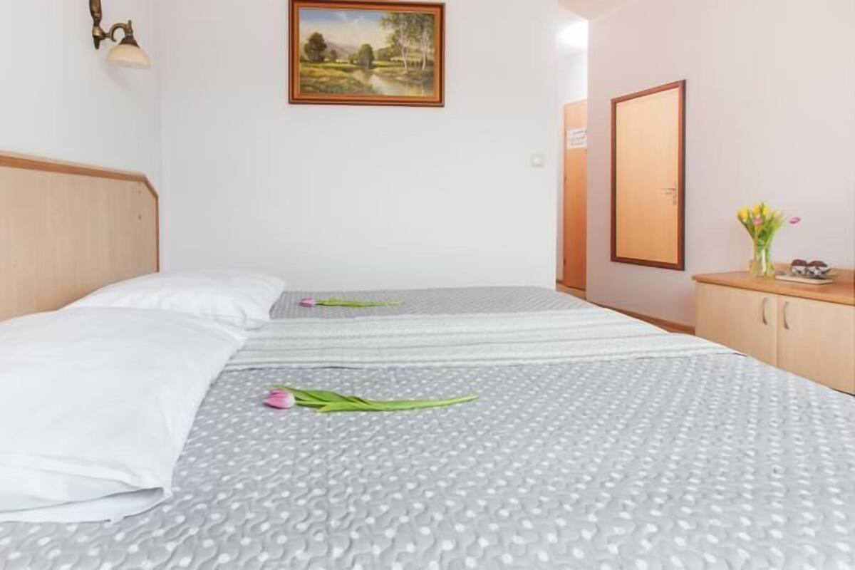 Une chambre d’hôtel avec deux lits, une tête de lit en bois, un tableau au mur, un miroir et une petite armoire sur laquelle est posé un vase de fleurs.