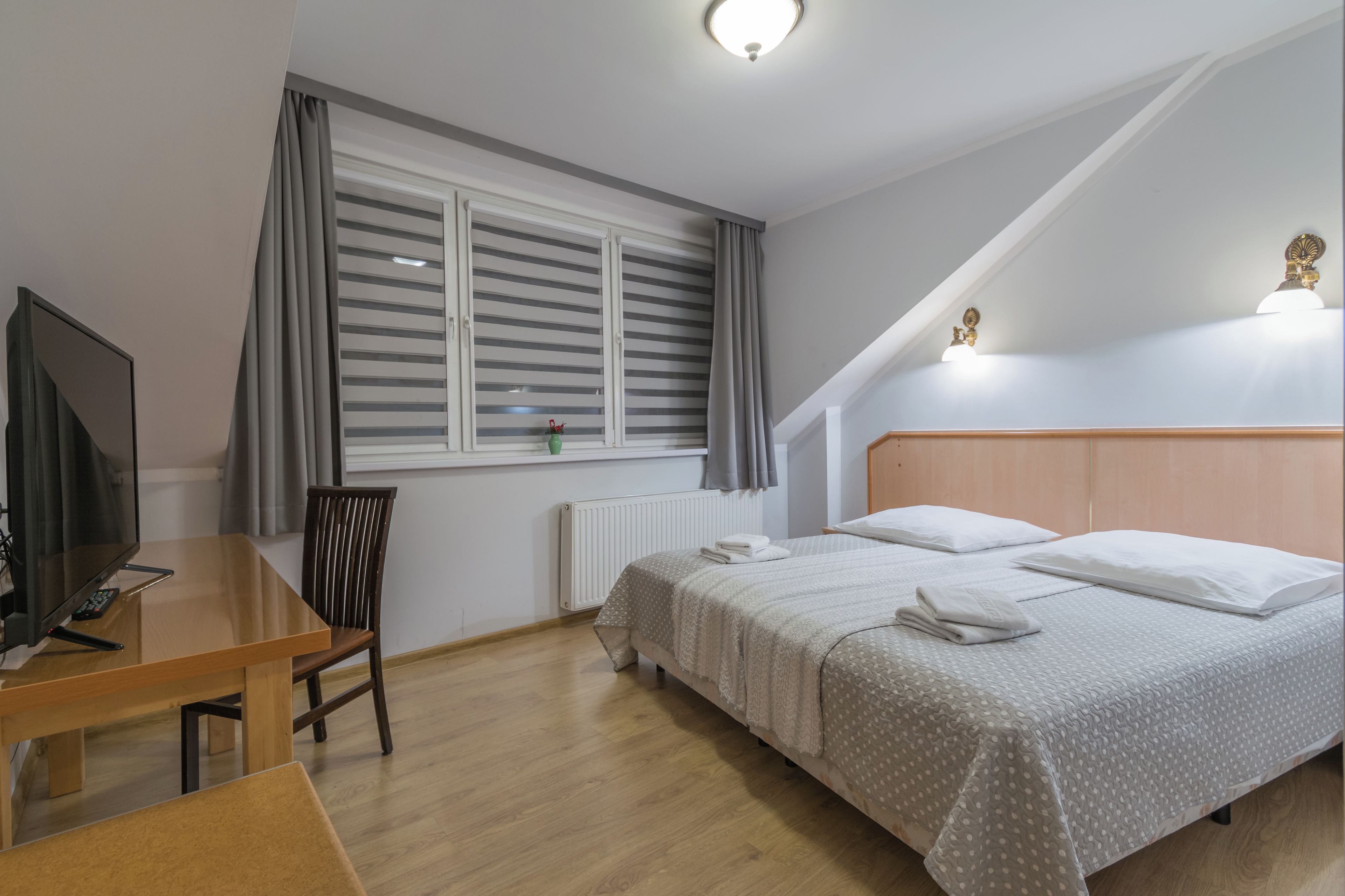 Un dormitorio con cama, escritorio, silla, televisor y ventana con cortinas.