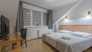 Un dormitorio con cama, escritorio, silla, televisor y ventana con cortinas.