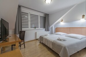 Un dormitorio con cama, escritorio, silla, televisor y ventana con cortinas.