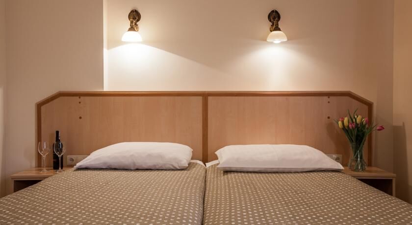 A double bed with a wooden headboard, two bedside tables, a vase with flowers, and wall-mounted lights.
