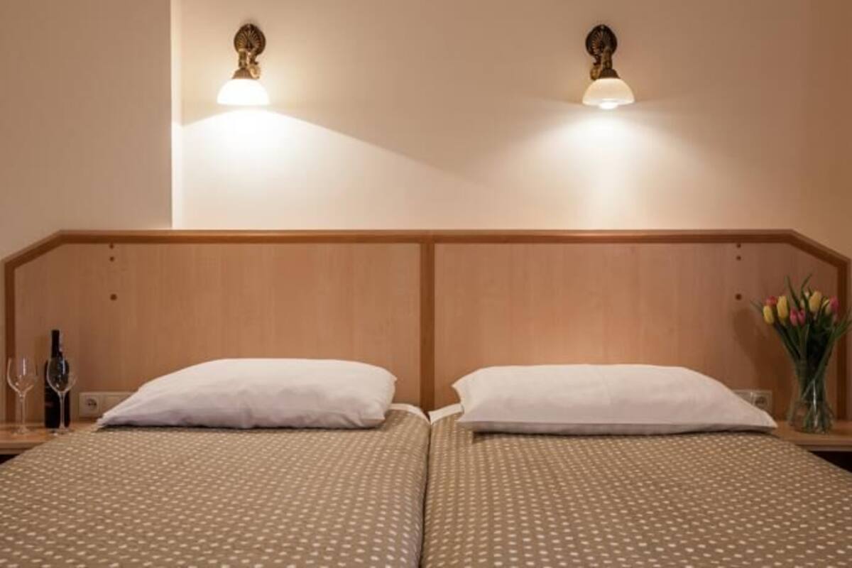 Un lit double avec une tête de lit en bois, deux tables de chevet et des lampes fixées au mur.
