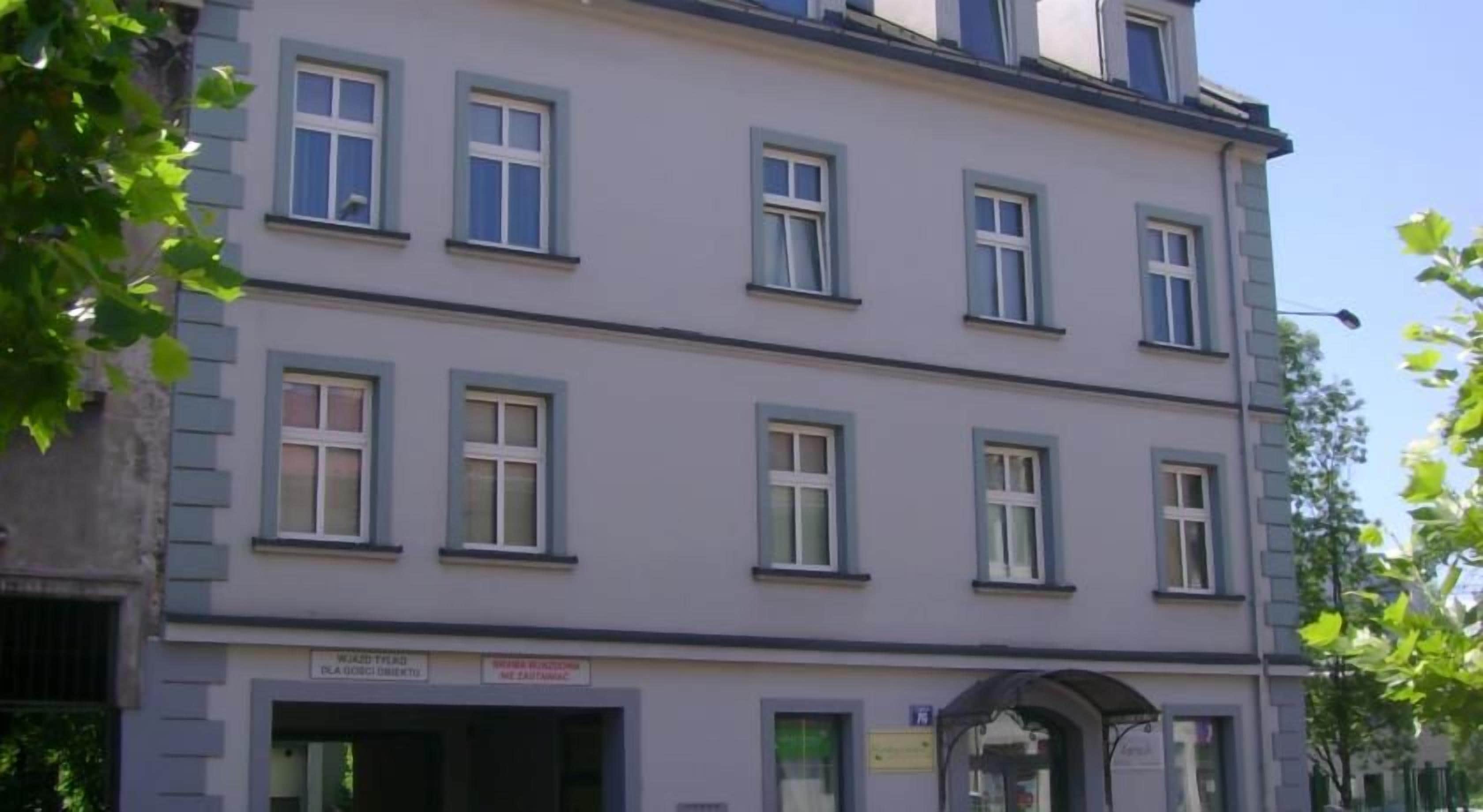 Um edifício com vários andares, fachada plana, diversas janelas e entrada no nível da rua com uma placa.