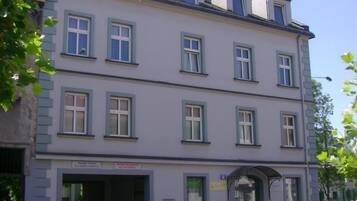 Um edifício com vários andares, fachada plana, diversas janelas e entrada no nível da rua com uma placa.
