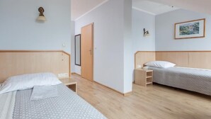 A hotel room with two beds, wooden headboards, a small bedside table, a nightstand, a wall-mounted lamp, and a framed picture on the wall.