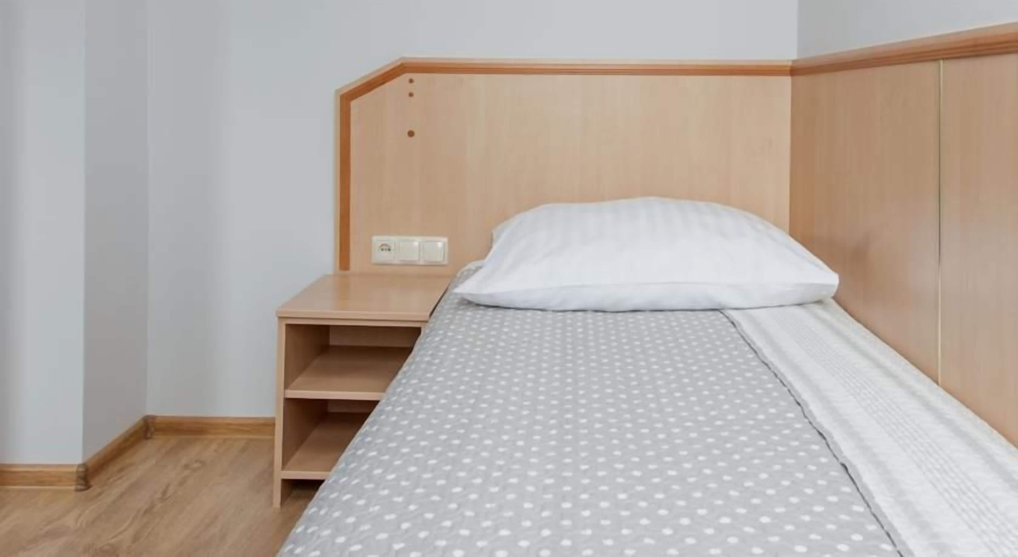 Un dormitorio con una cama, una mesita de noche de madera y un estante fijado a la pared.