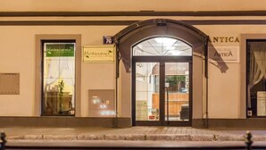 Fachada de edifício com uma grande entrada em arco, uma placa com o número 76 e duas vitrines visíveis com sinalização.