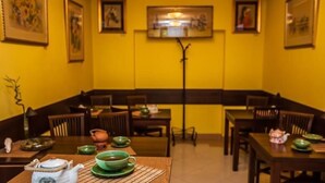A dining area with yellow walls, wooden tables, and chairs. There are green teacups and a teapot on the tables.