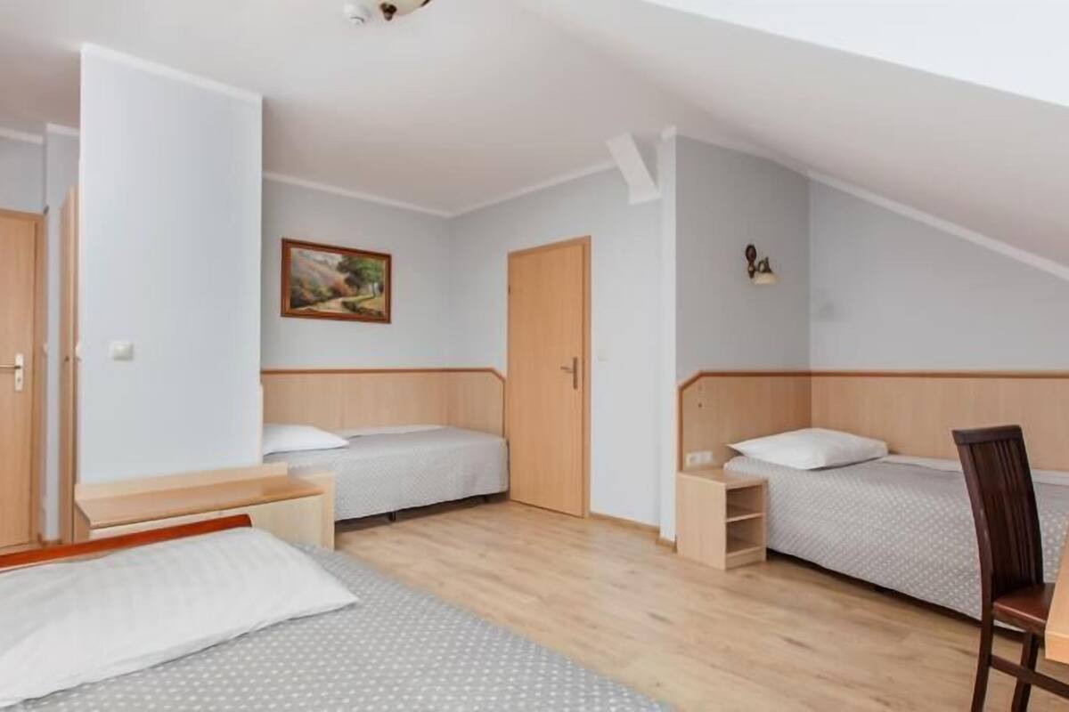 Une petite pièce bien éclairée, avec deux lits simples, un bureau en bois et une chaise.