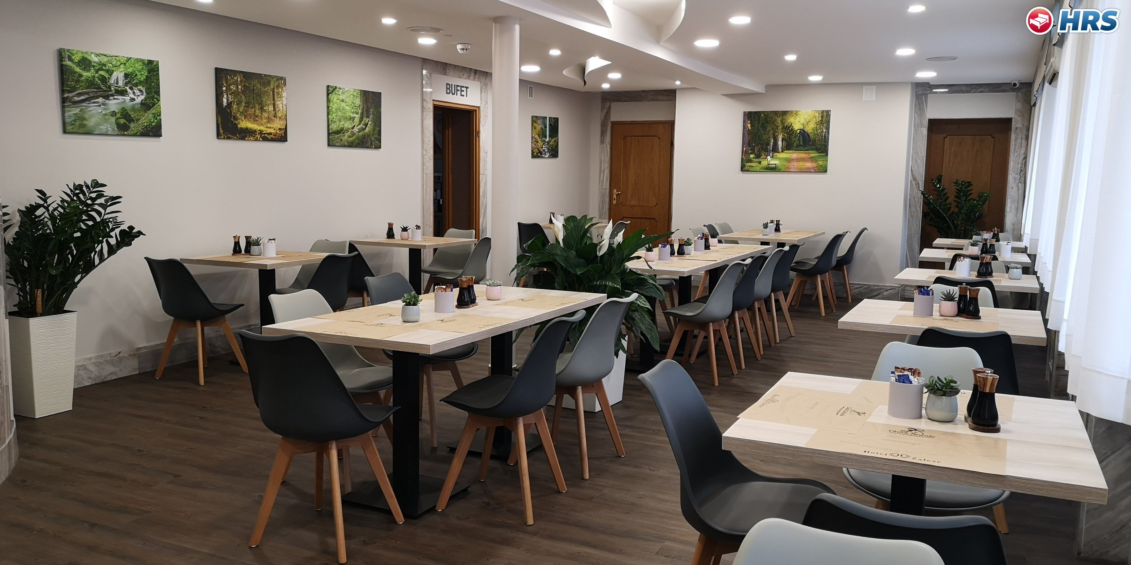Un salón de conferencias con varias mesas y sillas, suelo de madera y obras de arte colgadas en la pared.