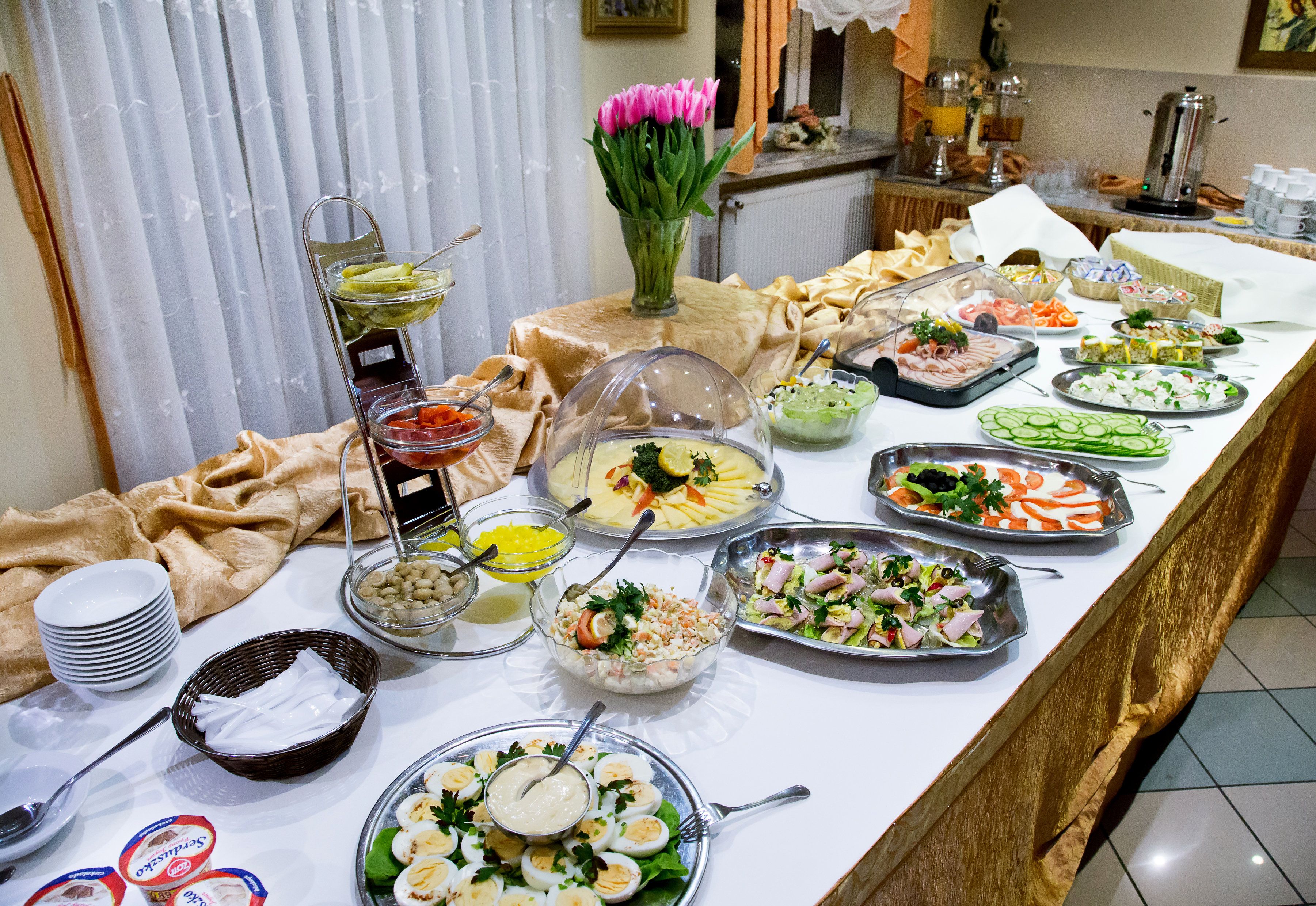 Una mesa de buffet con diversos alimentos y un florero con flores rosas.