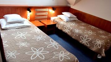 Habitación doble con dos camas individuales, cada una con una colcha de motivos florales. Tiene un cabecero de madera, una mesita de noche y un aplique de pared sobre las camas.