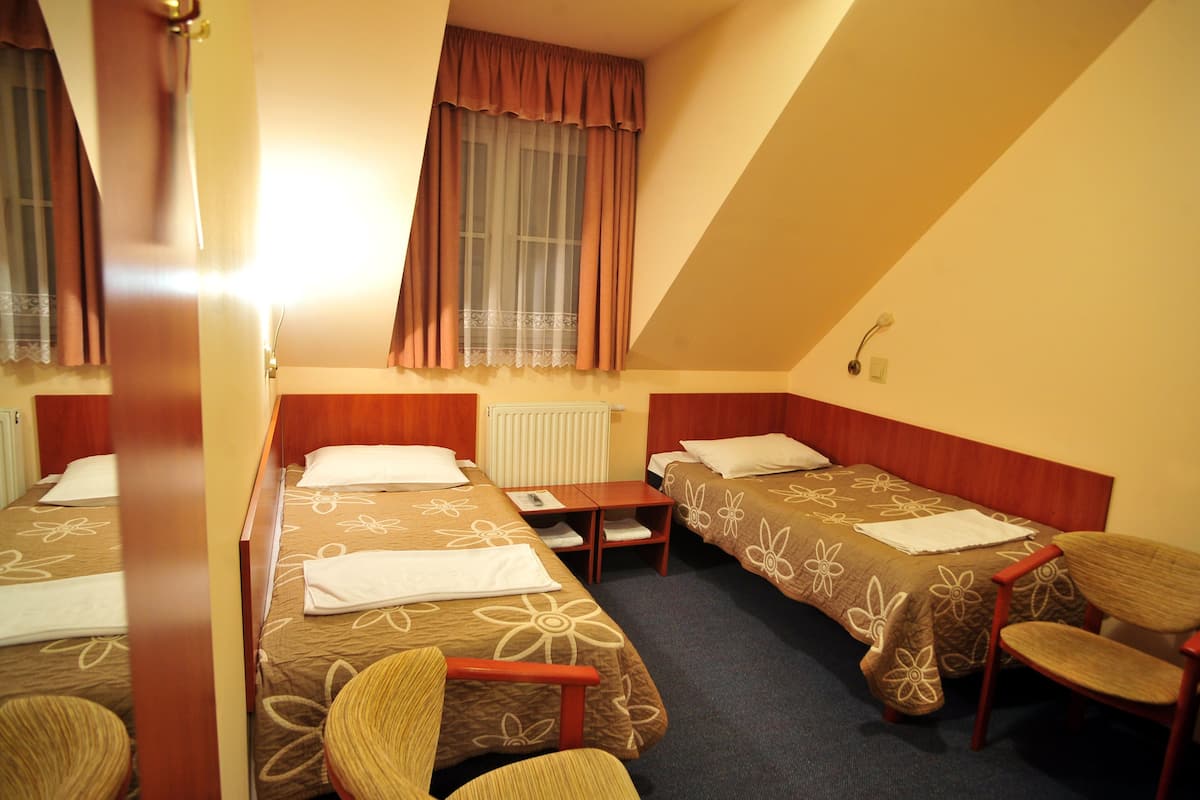 A hotel room with two single beds, a small table, two chairs, and a window with curtains.