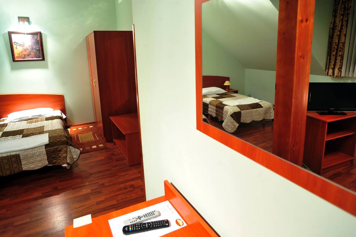 A hotel room with a bed, a desk with a remote control, a television, and a mirror reflecting the room.