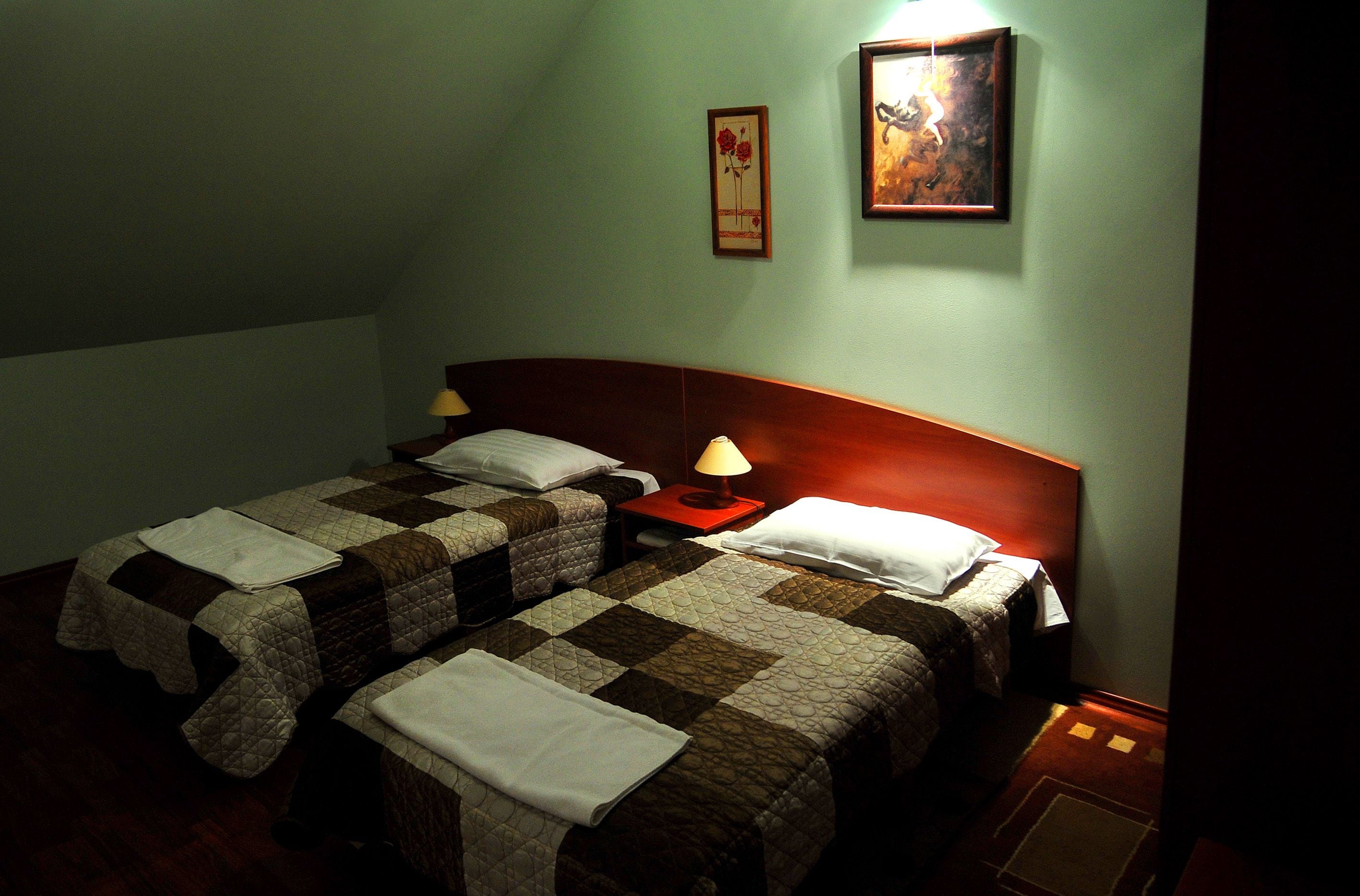 A room with two beds, a nightstand with a lamp, and a framed picture on the wall.