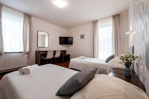 A hotel room with two beds, a desk, a chair, a flat-screen TV, and a vase with flowers.