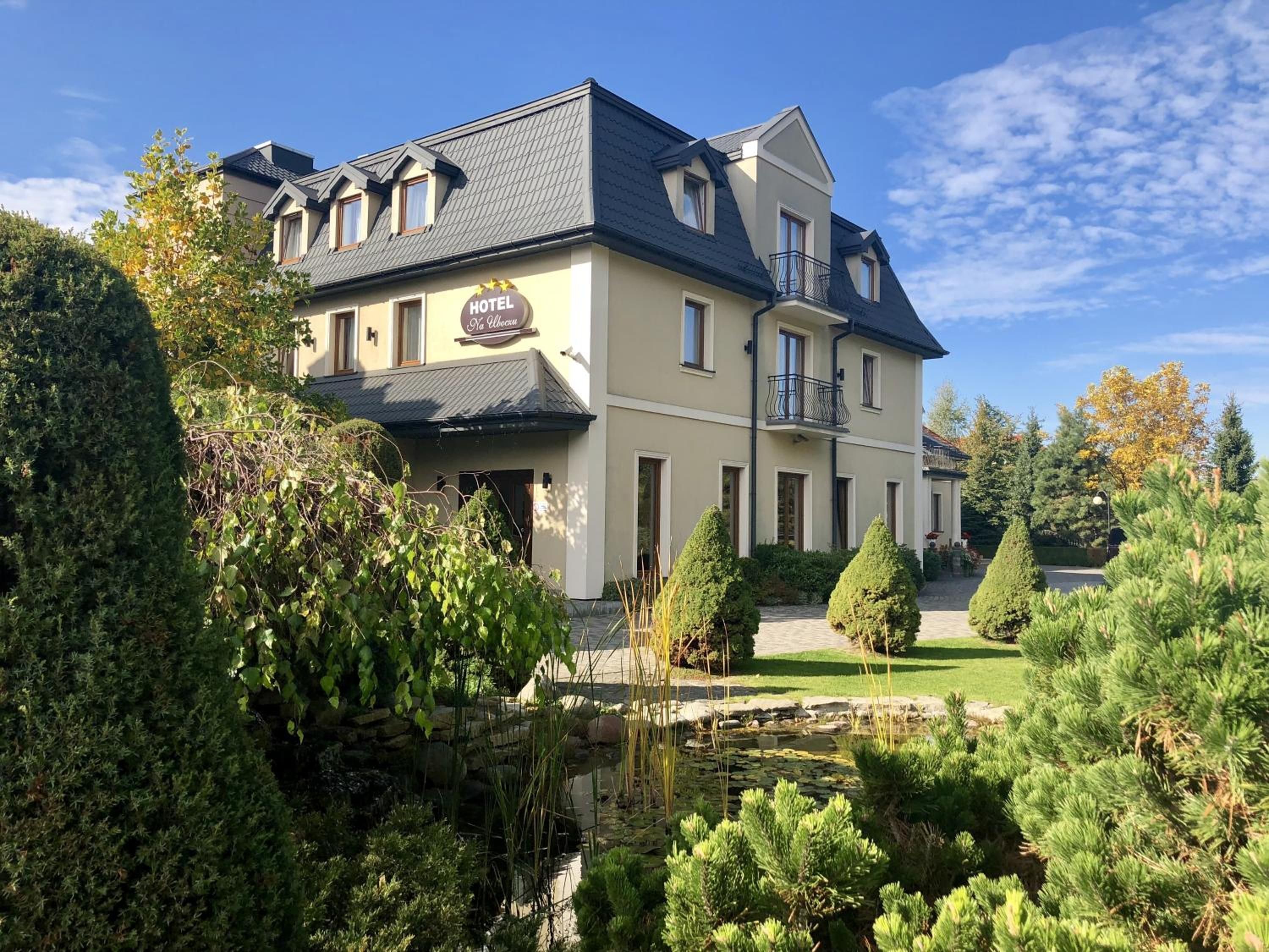 A two-story hotel with a balcony, a pond, and well-maintained gardens.