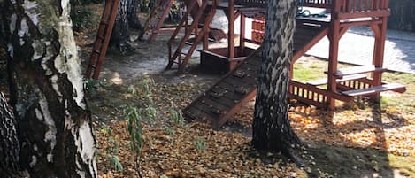 A wooden play structure in a wooded area with trees and a clear sky.