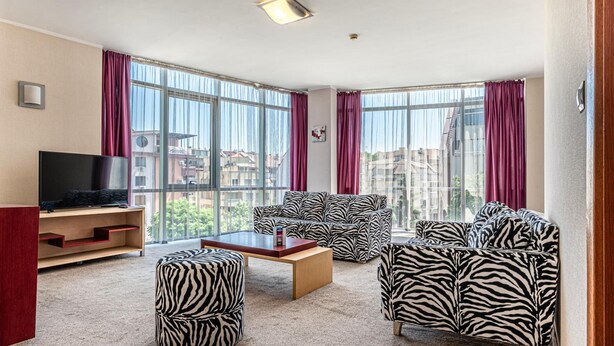 A modern living room with a large window, a flat-screen TV, and zebra-patterned furniture.