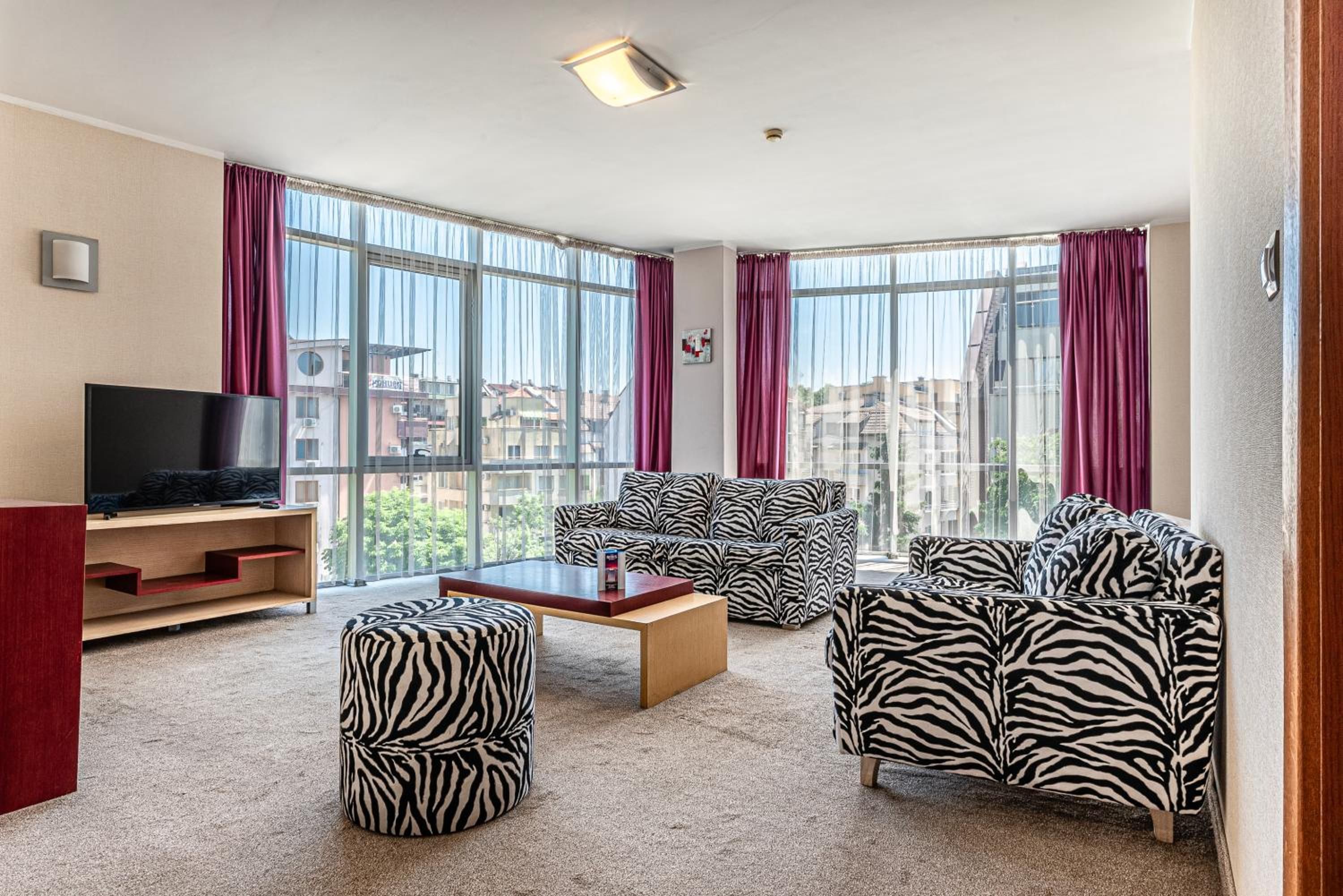 A modern living room with a large window, a flat-screen TV, and zebra-patterned furniture.