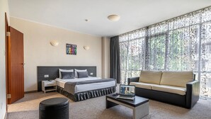 A hotel room with a bed, a sofa, a coffee table, and a window with curtains.