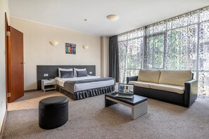 A hotel room with a bed, a sofa, a coffee table, and a window with curtains. - Hotel Noris (Plovdiv)