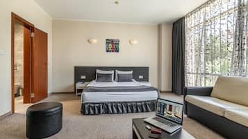 A hotel room with a bed, a sofa, a desk with a laptop, and a window with curtains.