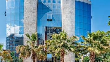 A modern building with a glass facade, palm trees in the foreground, and a clear blue sky.