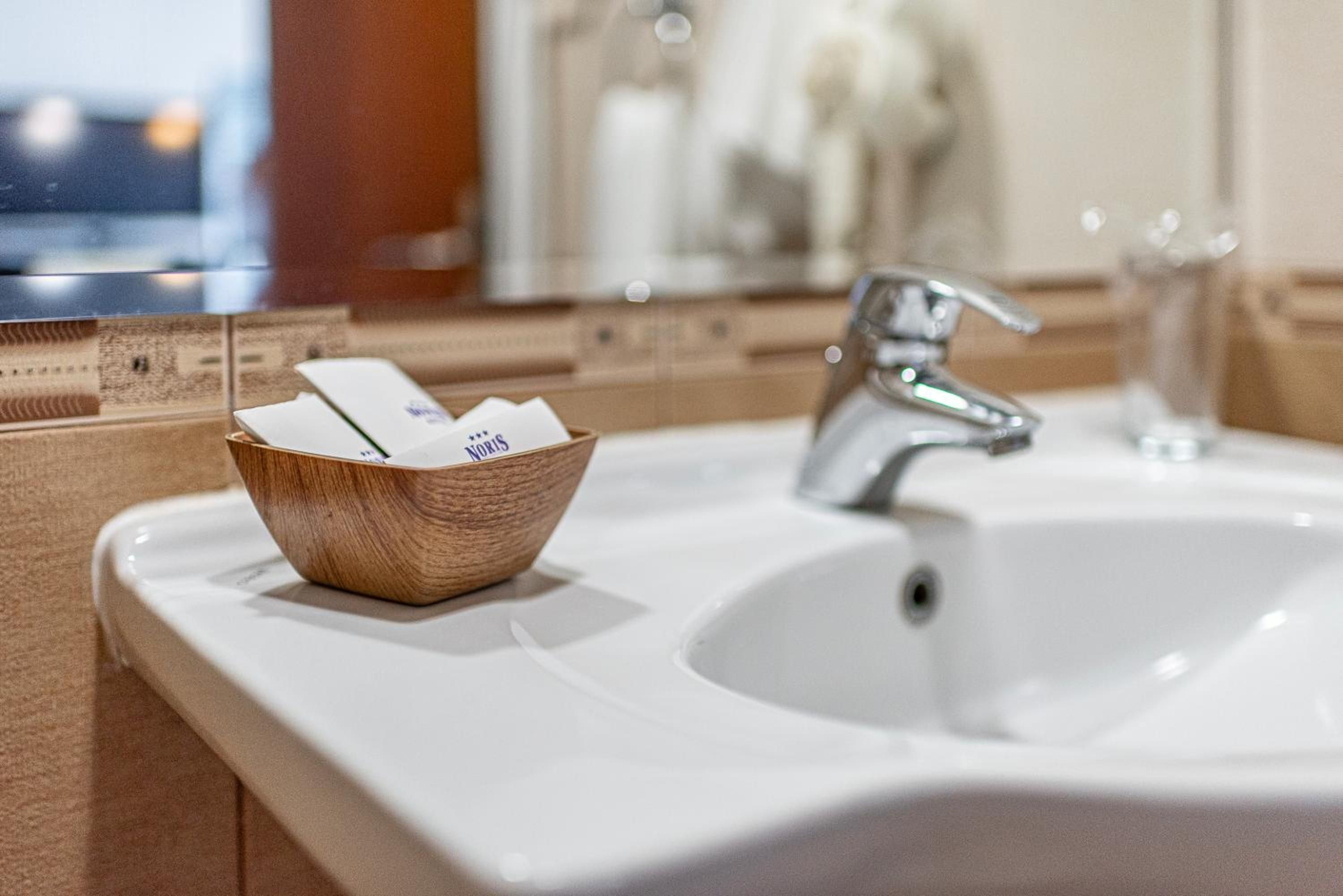 A bathroom with a wooden bowl containing toiletries, a white sink, and a mirror.