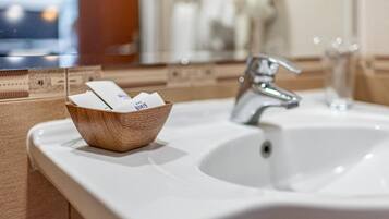 A bathroom with a wooden bowl containing toiletries, a white sink, and a mirror.
