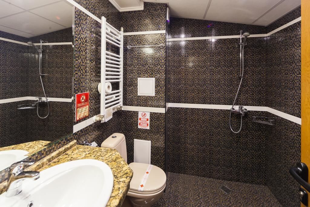 Un baño con lavamanos de encimera de granito, inodoro y zona de ducha con puerta de cristal.