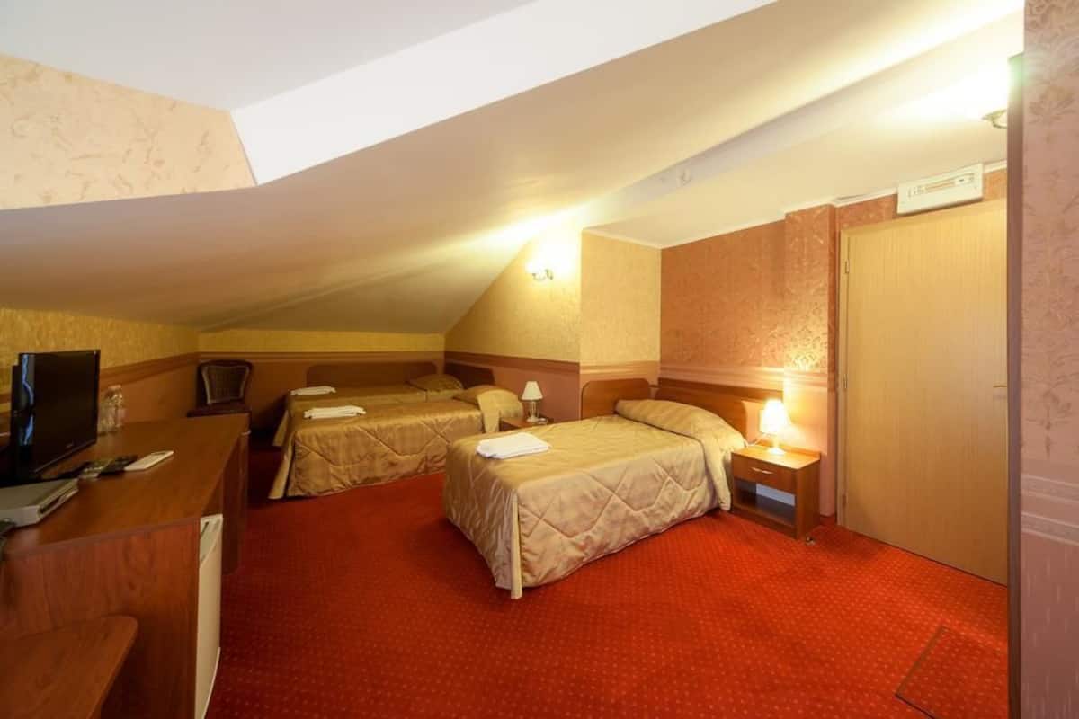 A hotel room with two beds, a desk with a television, and a red carpeted floor.