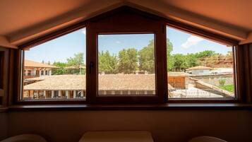 Ein Zimmer mit einem großen Fenster und Blick auf ein Wohngebiet mit Ziegeldächern und Bäumen.