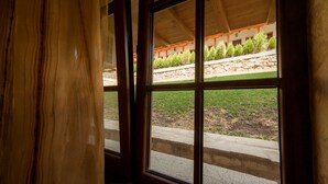 Une fenêtre donnant sur un jardin et un bâtiment doté d’un mur en pierre et de poutres en bois.