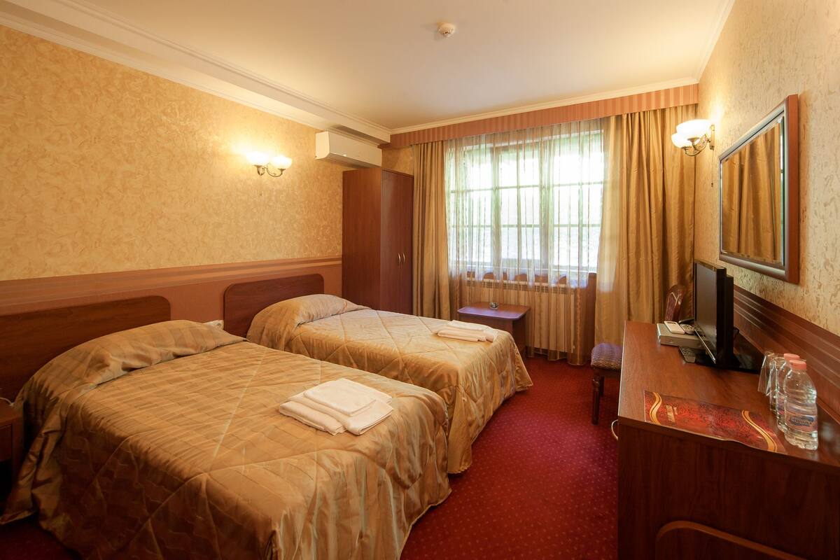 A hotel room with two beds, a desk, a chair, a mirror, and a window with curtains.