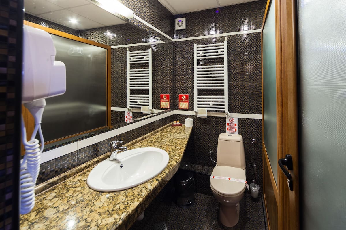 A bathroom with a granite countertop, a white sink, a mirror, a toilet, and a towel rack.