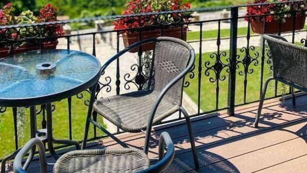 Une terrasse avec une table ronde en verre et deux chaises en osier, offrant une vue panoramique sur un paysage vallonné sous un ciel dégagé.