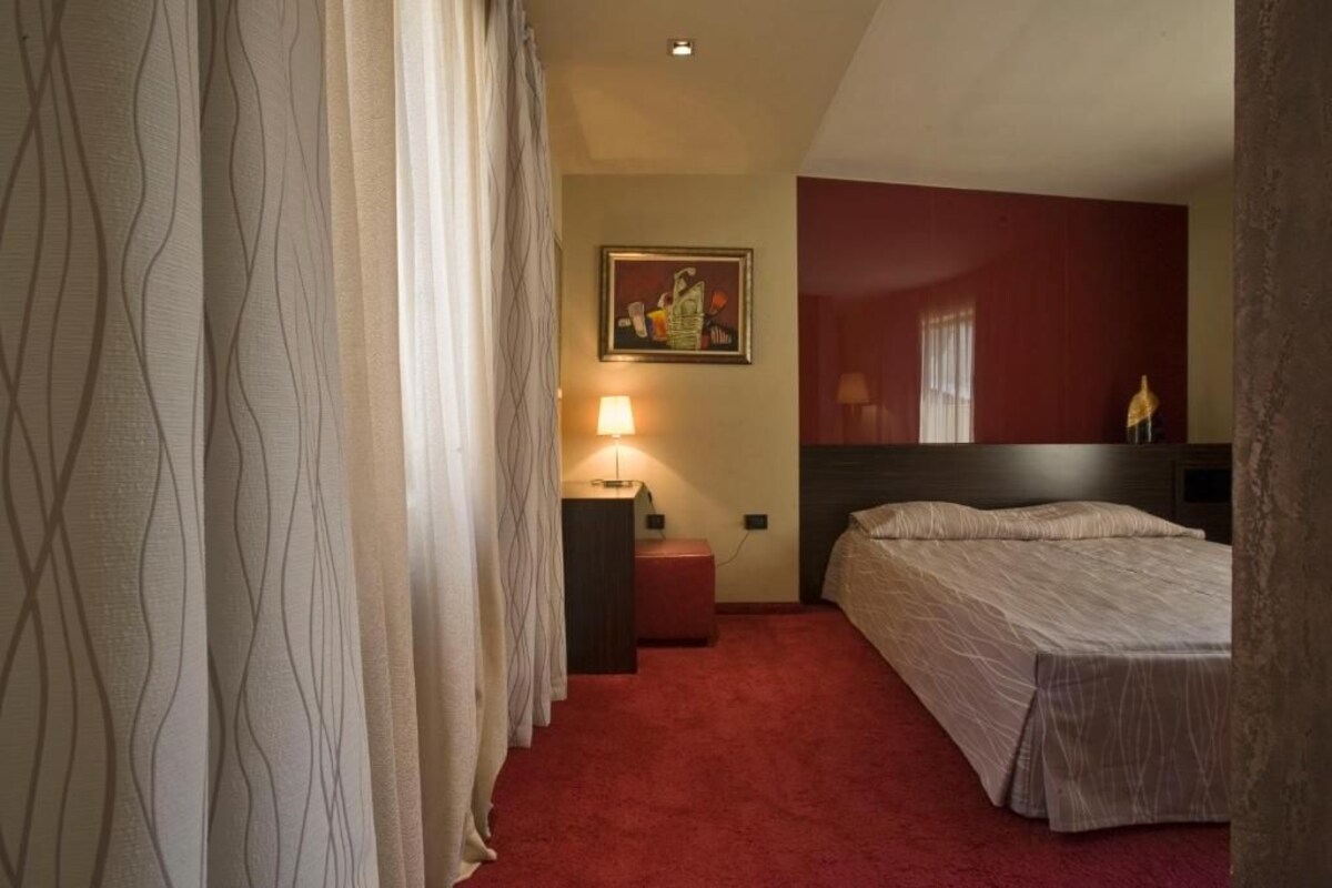 Habitació d'hotel amb un llit, una tauleta de nit, una làmpada i un quadre a la paret.