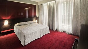 A bedroom with a bed, a nightstand, a mirror, and a window with curtains.