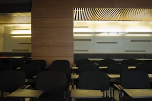 A classroom with desks and chairs arranged in rows, a wooden panel wall, and a slatted ceiling design.
