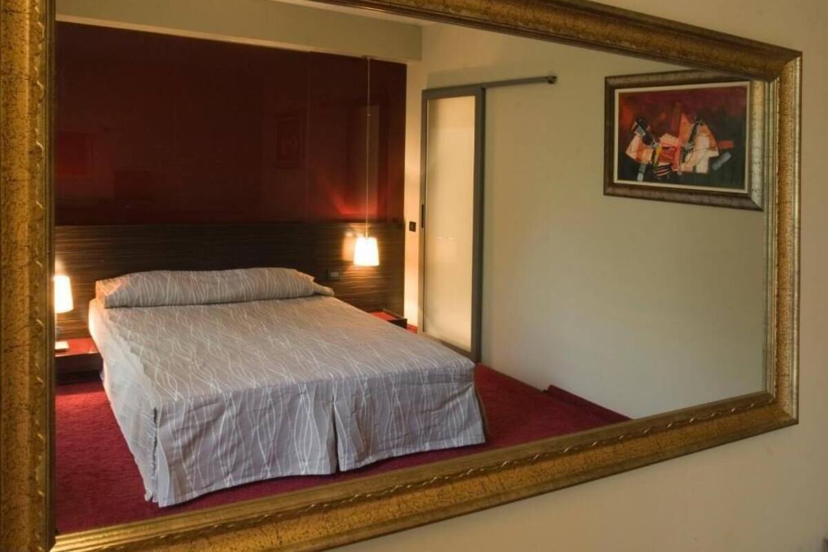 Une chambre d’hôtel avec un lit, un tableau accroché au mur et un miroir qui reflète la pièce.